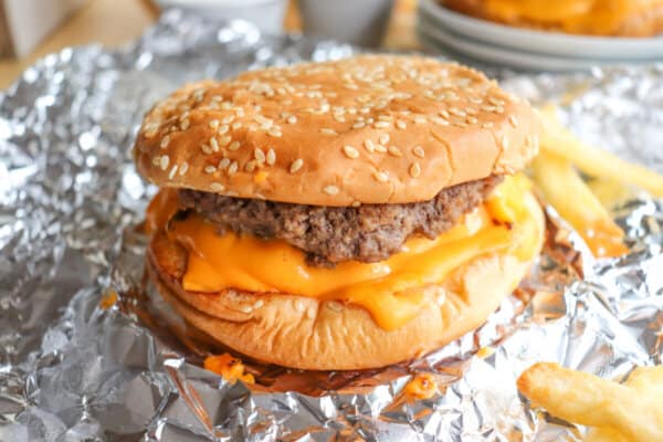 Copycat five guys burger with melted American cheese on a sesame seed bun on foil.