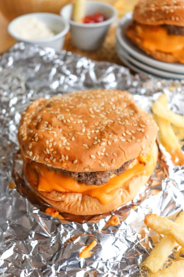 Copycat five guys burger with melted American cheese on a sesame seed bun on foil.