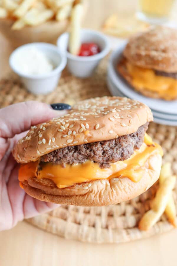 Copycat five guys burger with melted American cheese on a sesame seed bun being hand held.