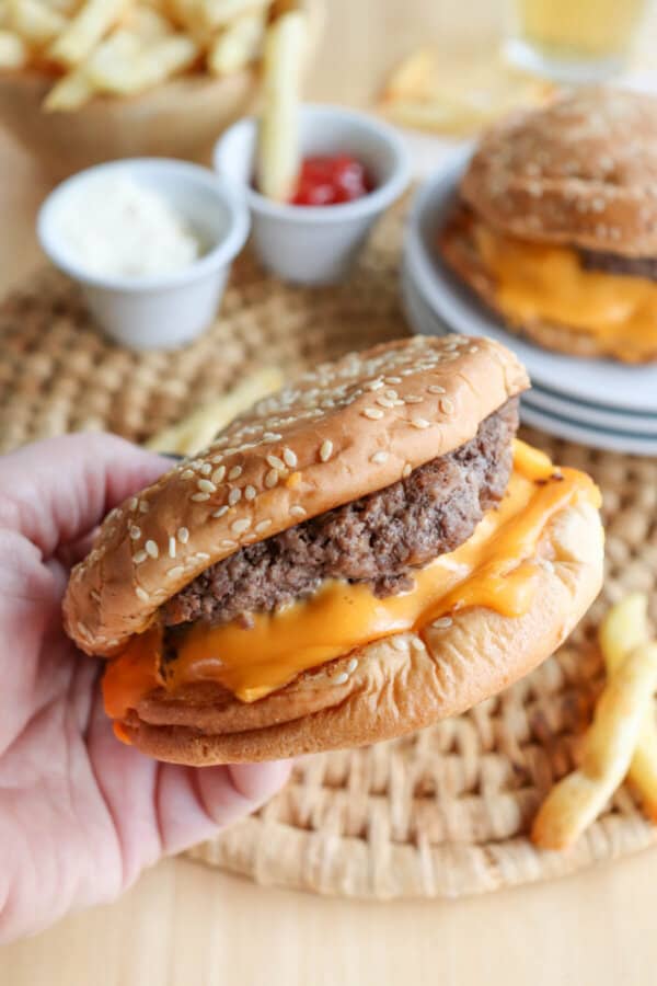 Copycat five guys burger with melted American cheese on a sesame seed bun being held in a hand.