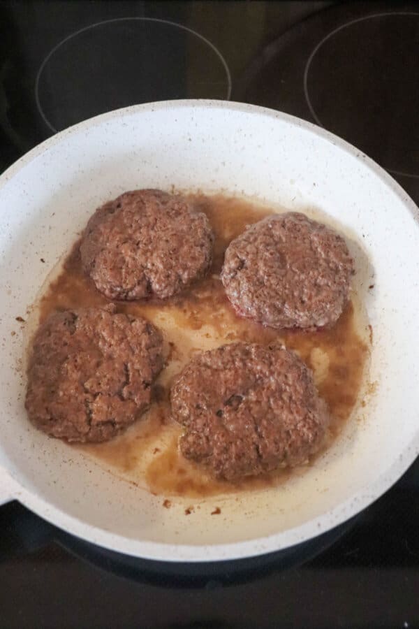 Five guys burgers on white skillet, cooked and surrounded by juices.