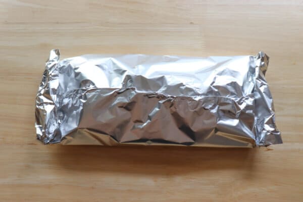 A packet of foil containing teriyaki chicken on a wood surface.