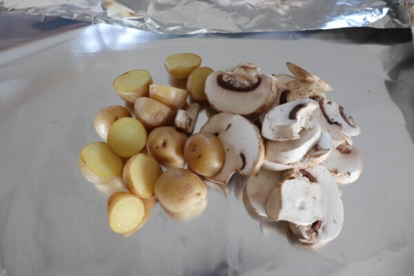 Sliced mushrooms and cut potatoes on a sheet of foil.