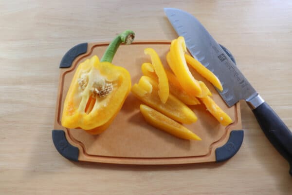 Yellow bell pepper sliced on a cutting board with a knife.