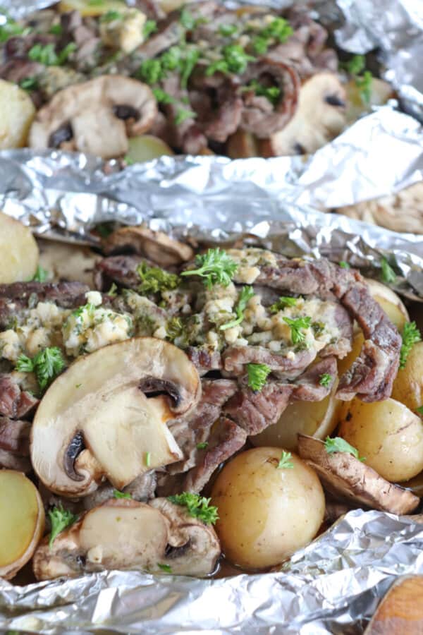 Close up of steak, sliced mushrooms and baby yellow potatoes cooked in a foil packet with garlic butter and fresh parsley garnish.