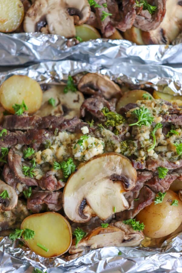 Steak, sliced mushrooms and baby yellow potatoes cooked in a foil packet with garlic butter and fresh parsley garnish.