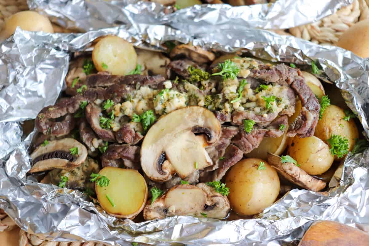 Steak, sliced mushrooms and baby yellow potatoes cooked in a foil packet with garlic butter and fresh parsley garnish.