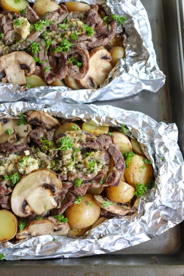 Steak, sliced mushrooms and baby yellow potatoes cooked in a foil packet with garlic butter and fresh parsley garnish.
