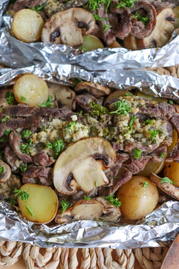 Steak, sliced mushrooms and baby yellow potatoes cooked in a foil packet with garlic butter and fresh parsley garnish.