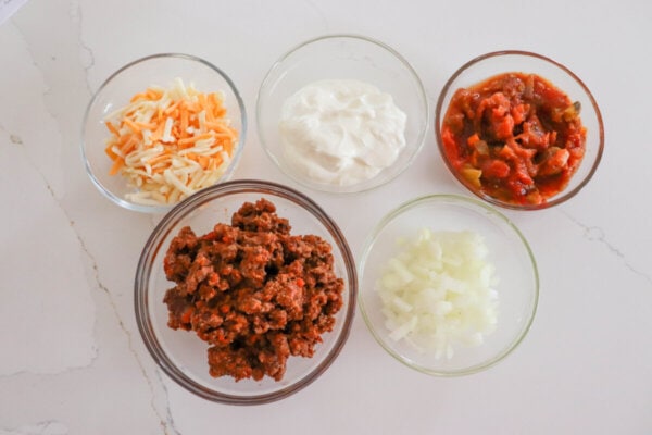 Taco hot dog ingredients in glass bowls.