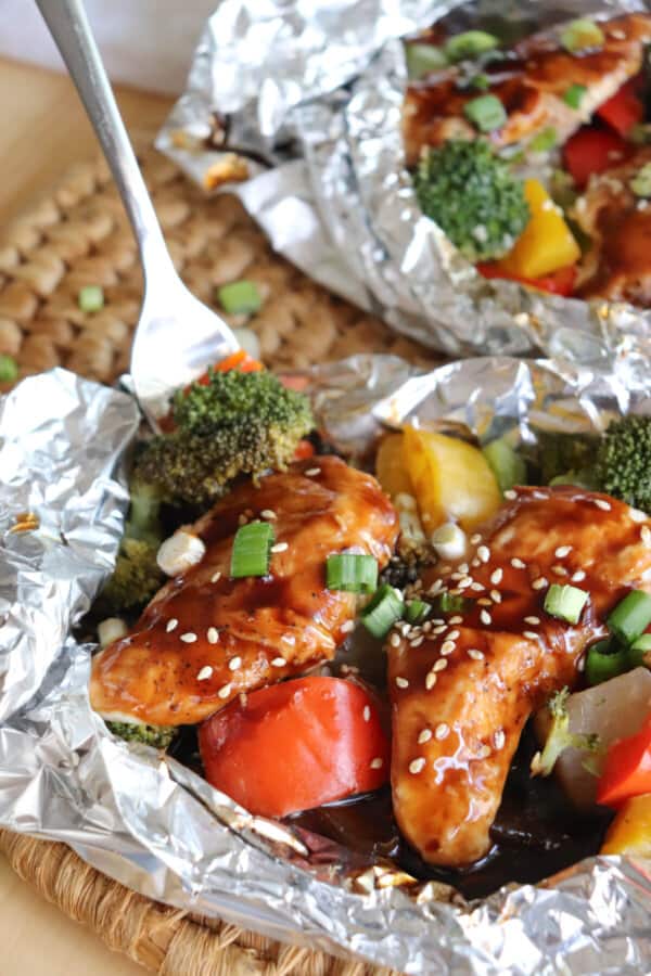 Chicken and vegetables covered in teriyaki sauce in a foil packet with a fork in it.