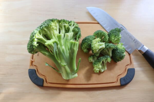 Broccoli cut into florets on a cutting board with a knife.