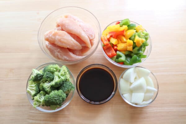 Teriyaki chicken ingredients in clear bowls on a wood background.