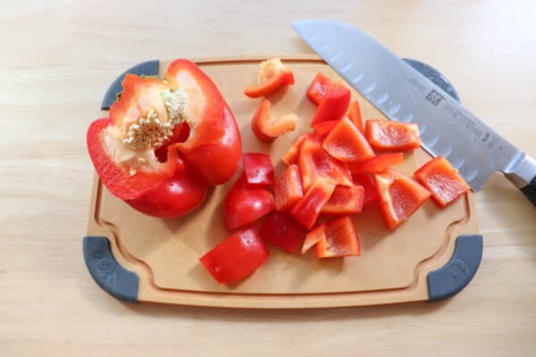 Red pepper cut into cubes on a cutting board with a knife.