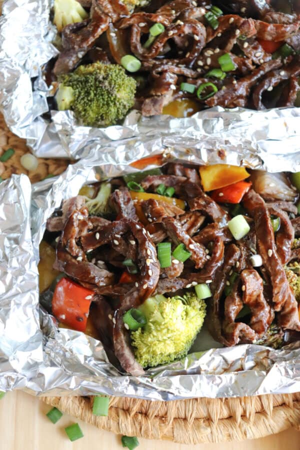 Steak on a bed of broccoli and diced bell peppers topped with teriyaki sauce, diced green onions and sesame seeds in a foil packet.