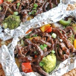 Steak on a bed of broccoli and diced bell peppers topped with teriyaki sauce, diced green onions and sesame seeds in a foil packet.