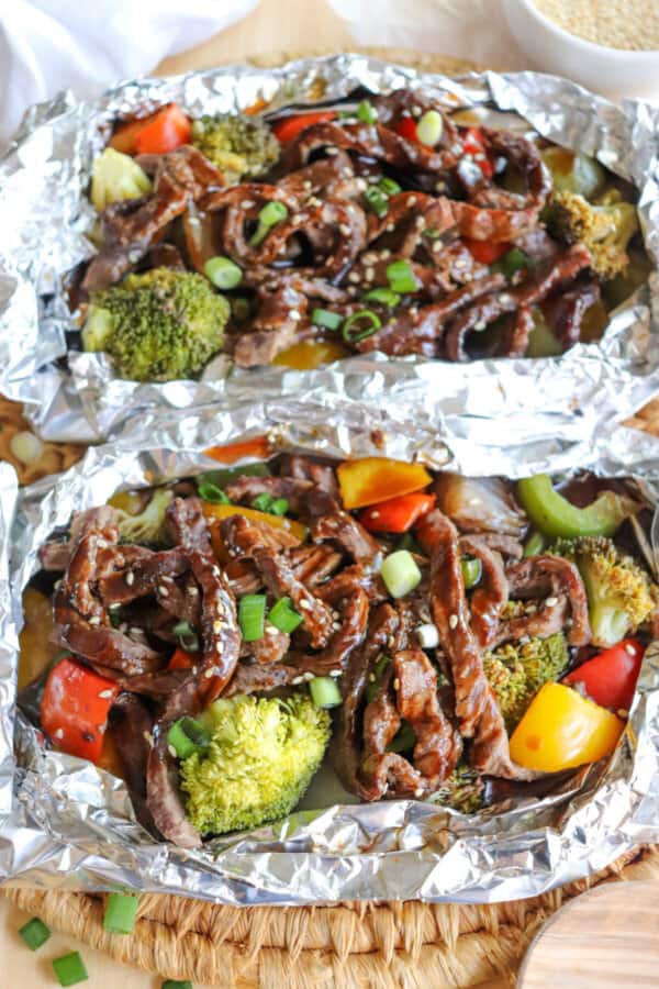 Steak on a bed of broccoli and diced bell peppers topped with teriyaki sauce, diced green onions and sesame seeds in a foil packet.