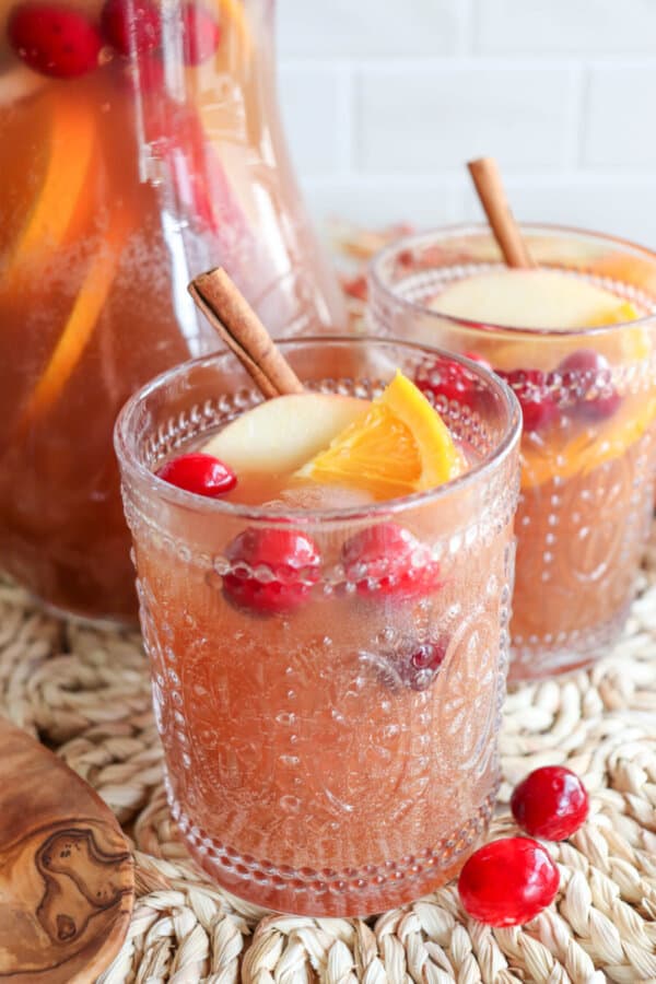 Thanksgiving punch in two filled glasses topped with apple slices, orange slices and cranberries.