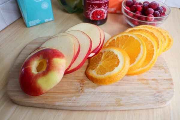 Sliced apple and orange on a wooden cutting board.