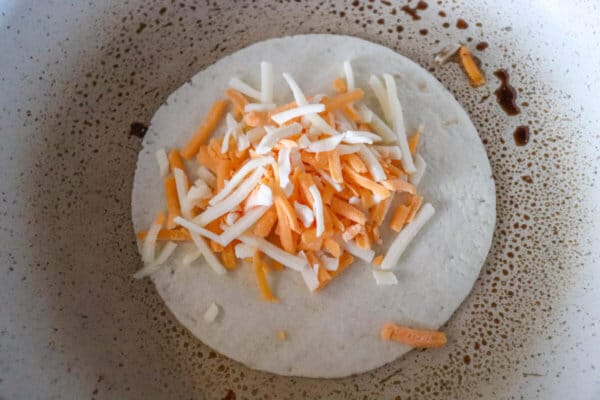 Tortilla with shredded cheese in skillet