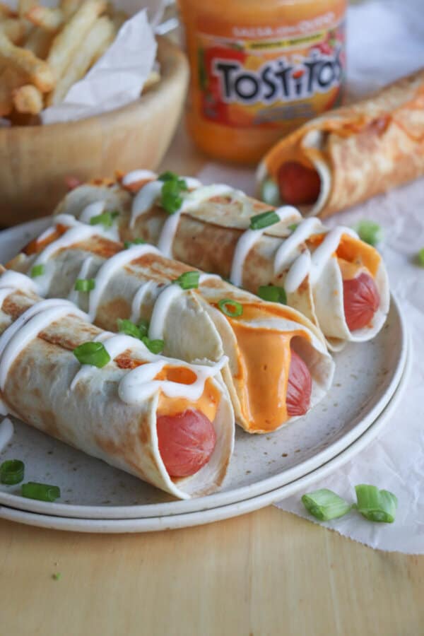 Three Hot Dog Taquitos on a cream plate with creama drizzle.