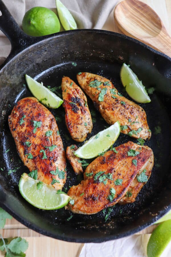 Chicken breasts blackened with seasoning, garnished with cilantro and lime wedges in a cast iron skillet.