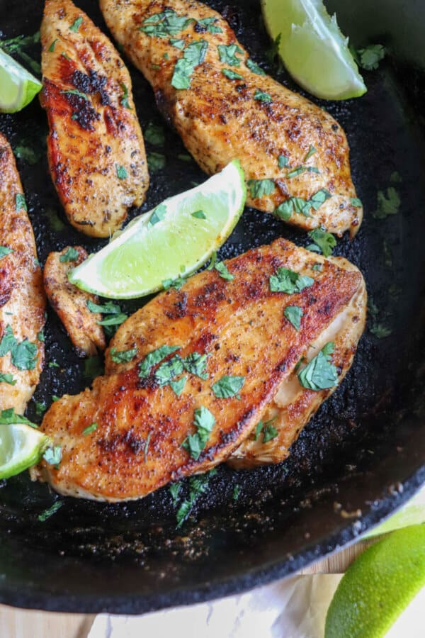 Chicken breasts blackened with seasoning, garnished with cilantro and lime wedges in a cast iron skillet.