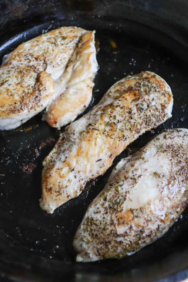 Cooked chicken breast with Italian seasoning in a cast iron skillet.