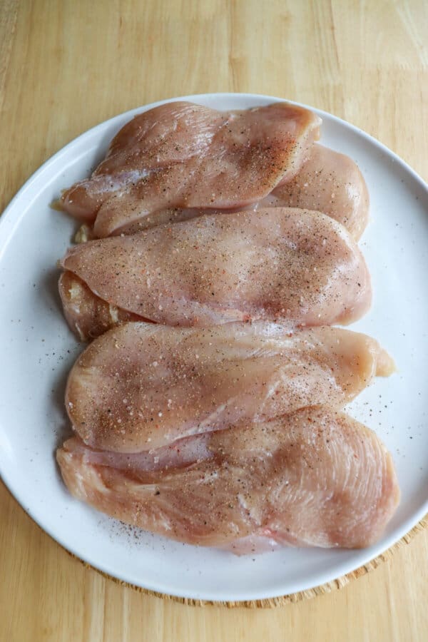 Raw chicken breast cut into cutlets seasoned with salt and pepper in a speckled plate.