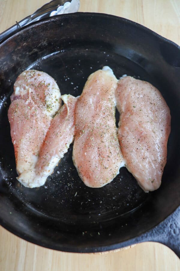 Raw chicken breast with seasoning in a cast iron skillet.