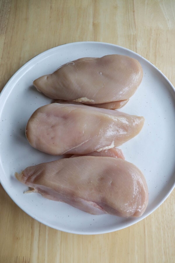 Three chicken breasts on a speckled plate.