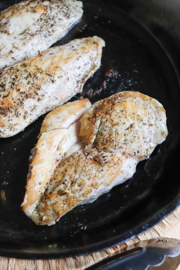Cooked chicken breast with Italian seasoning in a cast iron skillet.