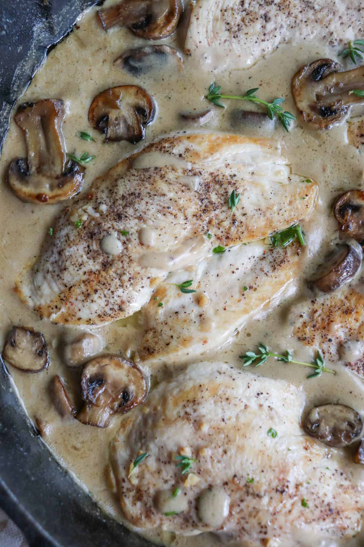 Cooked chicken breast covered in a cream sauce with mushrooms in a cast iron skillet.