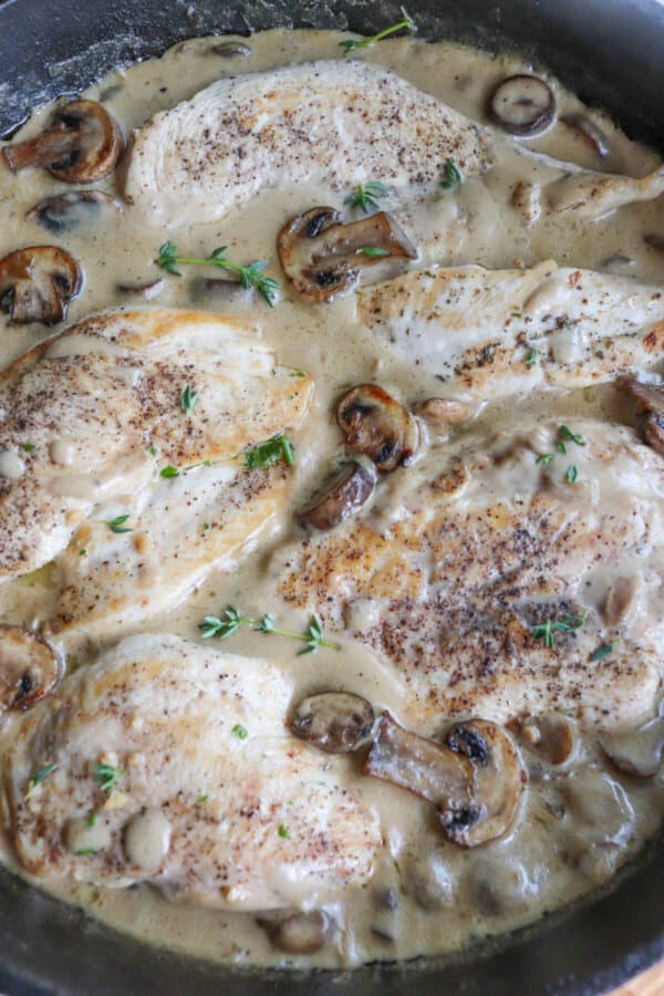 Close up of cooked chicken breast covered in a cream sauce with mushrooms in a cast iron skillet.