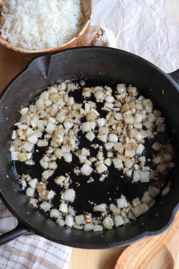 Diced garlic and onion cooking in a cast iron skillet.