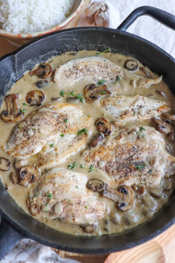 Cooked chicken breast covered in a cream sauce with mushrooms in a cast iron skillet.