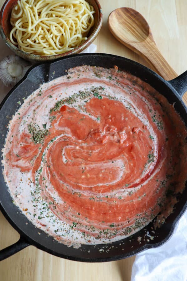 Tomato sauce swirled with cream and seasoning in a cast iron skillet.