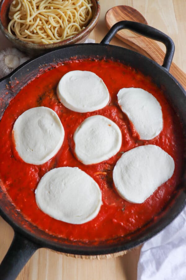 A cast iron pan with tomato sauce topped with rounds of mozzarella cheese.