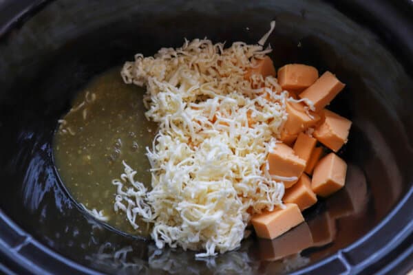 Salsa verde, cubed Velveeta and shredded Monterrey Jack cheese in a black crockpot.