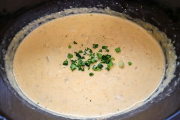 Creamy light orange cheese dip with diced jalapeno garnish in a black crockpot.