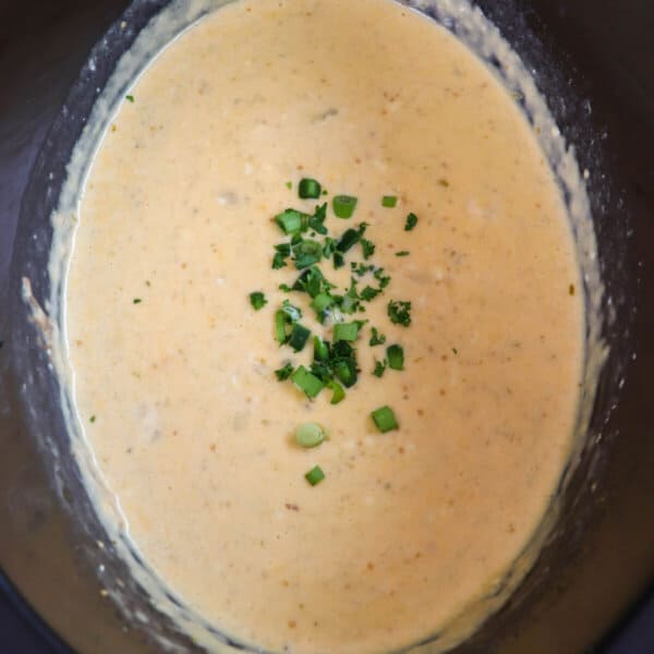 Creamy light orange cheese dip with diced jalapeno garnish in a black crockpot.