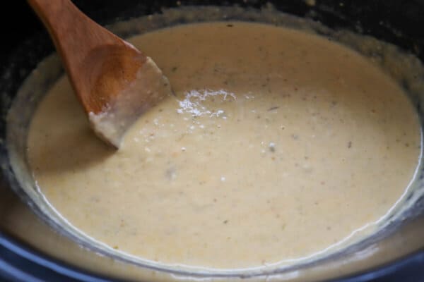 Creamy light orange cheese sauce in a black crockpot with a wooden serving spoon in it.