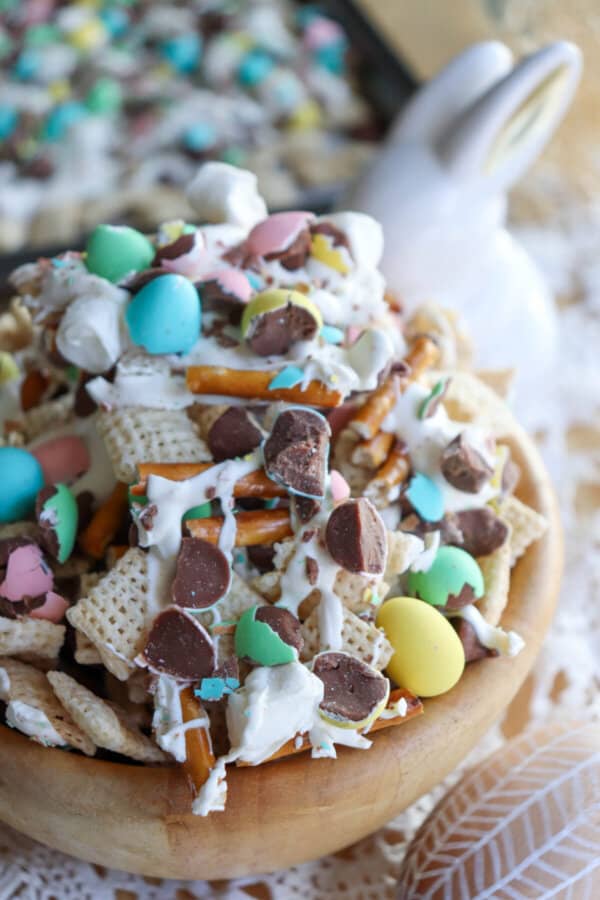 Easter snack mix with chex cereal, pretzels and chopped mini eggs drizzled with white chocolate in a wooden bowl.