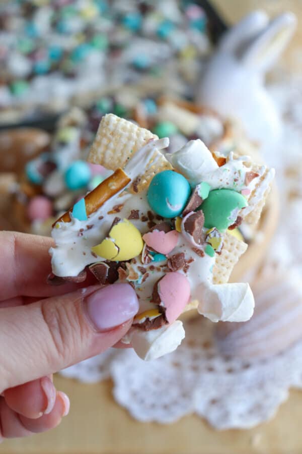 Easter snack mix with chex cereal, pretzels and chopped mini eggs drizzled with white chocolate held in a hand.