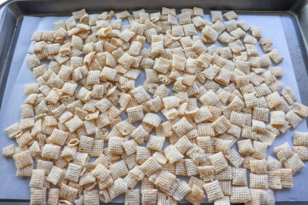 Chex cereal spread in one layer on a parchment paper lined baking sheet.
