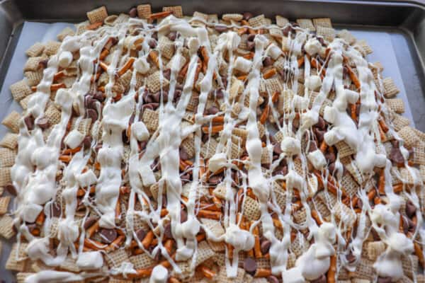 Chex snack mix with a drizzle of white chocolate all over it on a baking sheet.