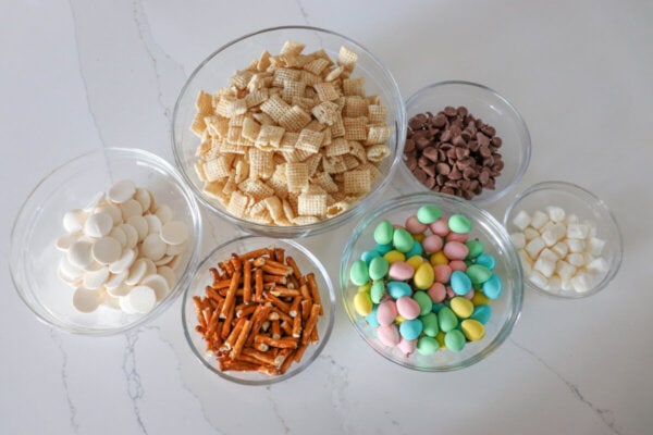 Easter snack mix ingredients in clear glass bowls.