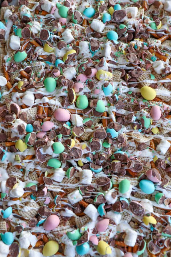 Easter snack mix with chex cereal, pretzels, marshmallows and chopped mini eggs drizzled with white chocolate on a cookie sheet.