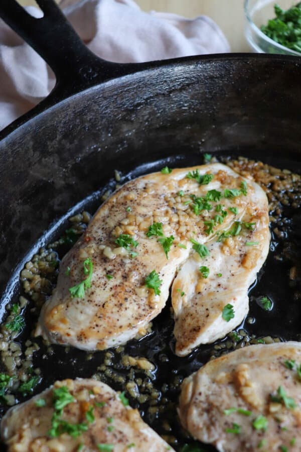 Close up of cooked chicken breast covered in melted butter and garlic in a cast iron skillet.