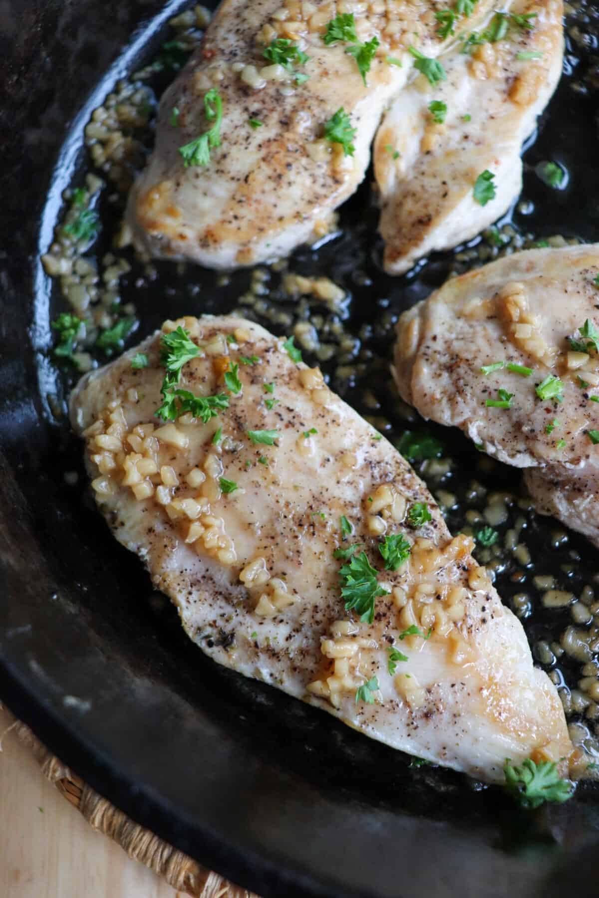 Cooked chicken breast covered in melted butter and garlic in a cast iron skillet.